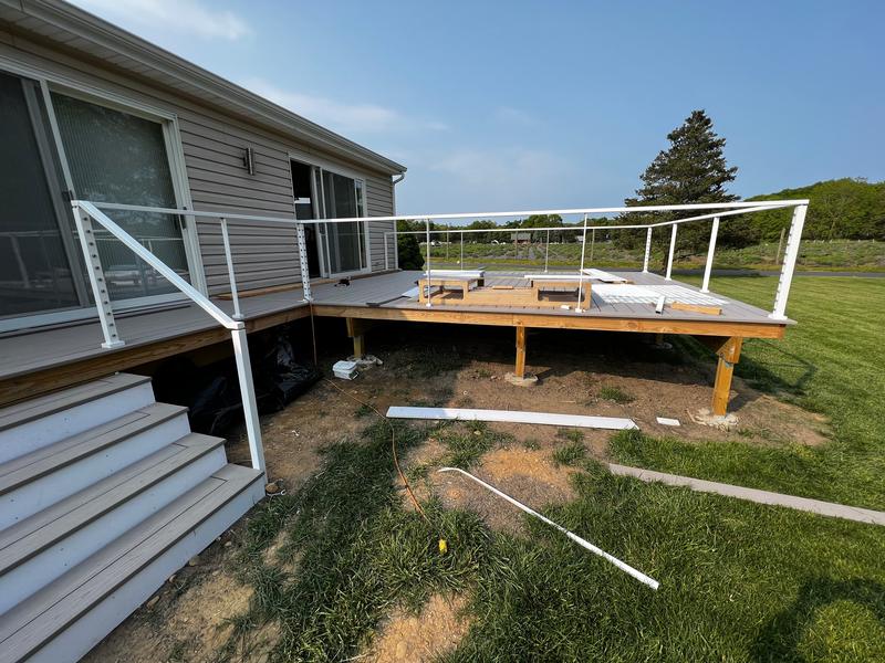 Deck mid-build, with composite boards partly laid and white cable-rail posts going up