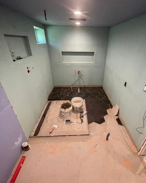 Bathroom mid-renovation with board on the walls, framed niches and the first black hexagon floor tiles laid