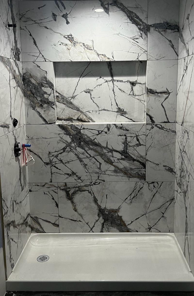 The same basement bathroom's shower: white slab tile with dramatic black veining on three walls, a long niche and a white shower pan