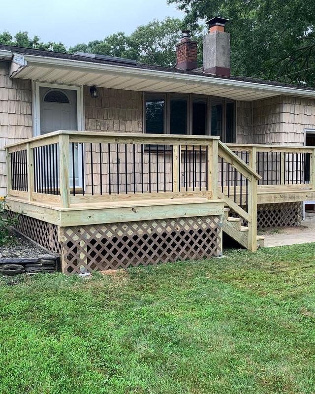 New wood front deck with black metal balusters, steps and a lattice skirt on a shingled house
